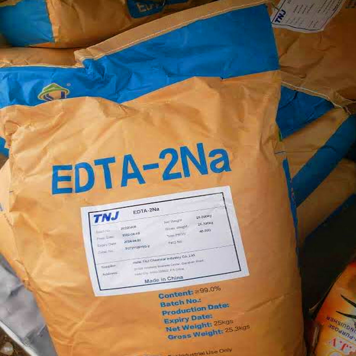 A large brown paper bag of EDTA-2Na chemical reagent with a white label and blue text, placed on top of blue and brown packaging bags.
