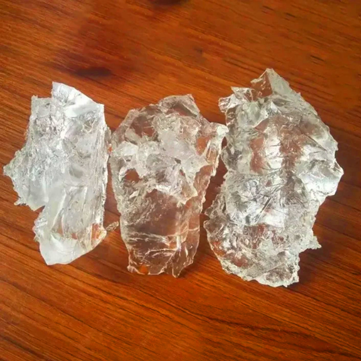 Three rough, translucent clear crystal or glass-like chunks arranged on a warm brown wooden surface.
